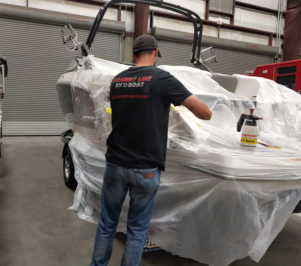 A worker masking off sections of a boat as preparation for painting